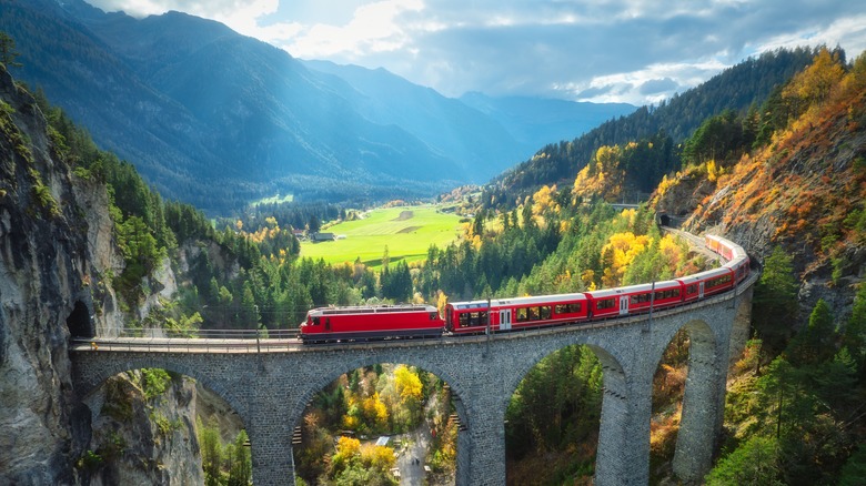 Red swiss train, on a high arched stone bridge, lush alpine slopes