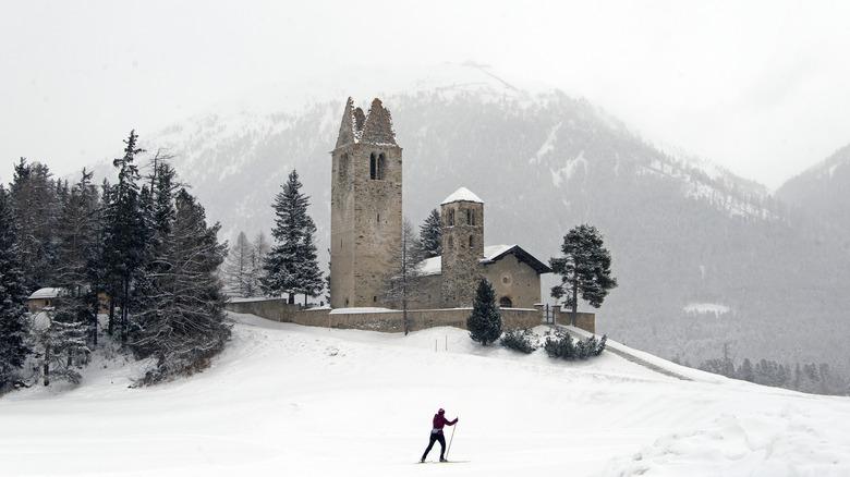 Man skiing on an empty snowy terrain with a medieval village church in the backdrop