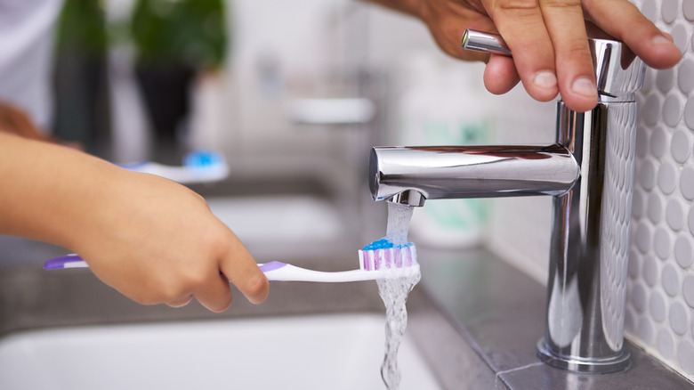 A person holding a toothbrush under a tap.