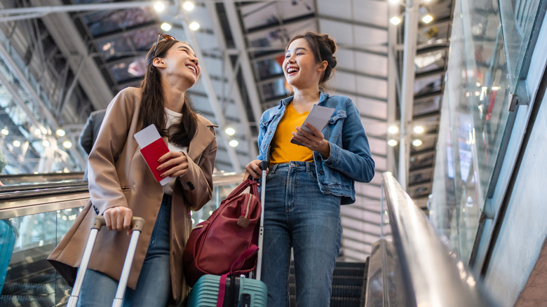 Two smiling women taking the airport escalator