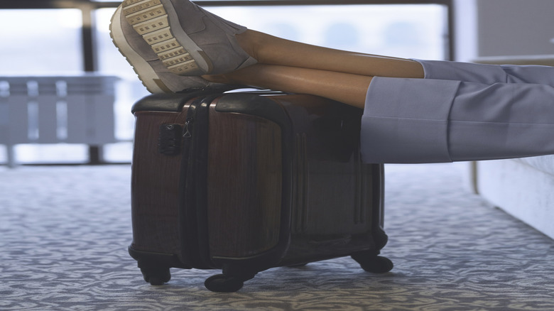 Person relaxing at airport gate putting their slip-on shoes on top of their luggage
