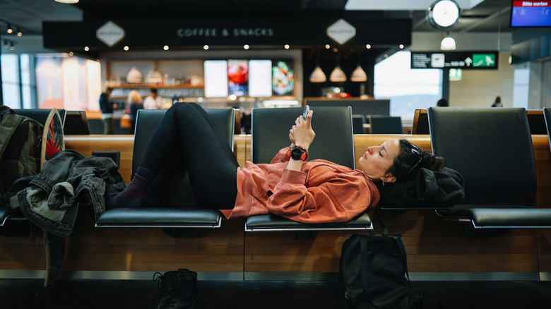 Woman relaxing at the airport, reading stuff on her smartphone, having a long layover.