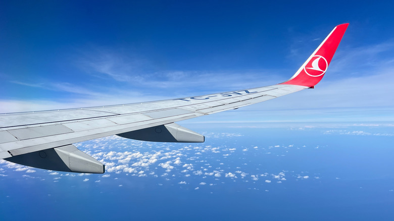 Wing of Turkish Airlines plane against a bright blue sky with just a few scattered clouds