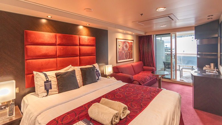 Balcony cabin of MSC Fantasia cruise ship, with red headbaord, red carpeting, and cream and brown accents