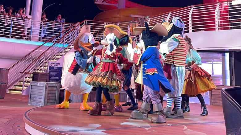 Disney characters including Donald, Minnie, Mickey, and Goofy gather onstage during Pirate Night on the Disney Wish cruise ship