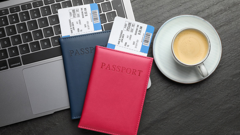 Flight tickets, passports, laptop and cup of coffee on dark textured table, flat lay