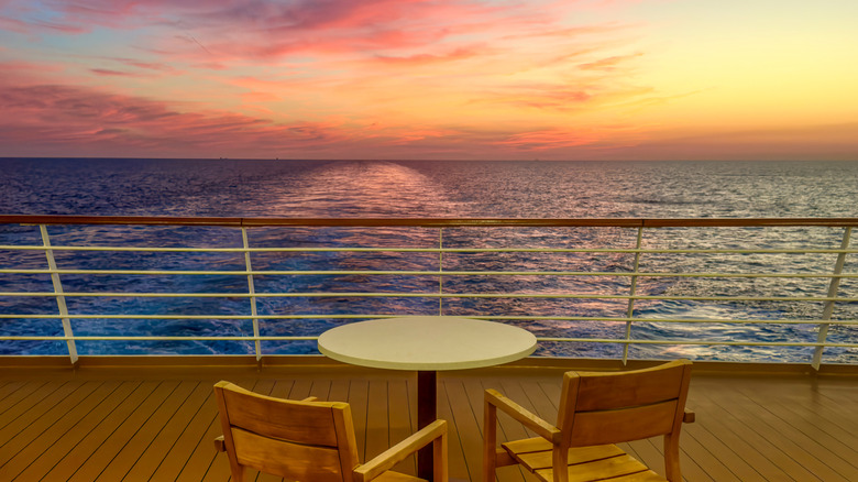 A table and chairs on the deck of a cruise ship with a spectacular sunset over the ocean in the background