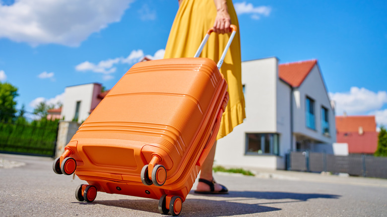 Woman in a yellow dress rolling an orange suitcase