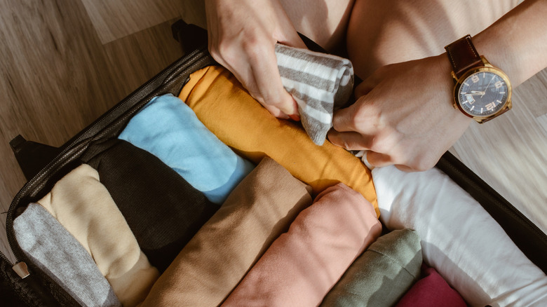 Person rolling clothes and packing them in a suitcase
