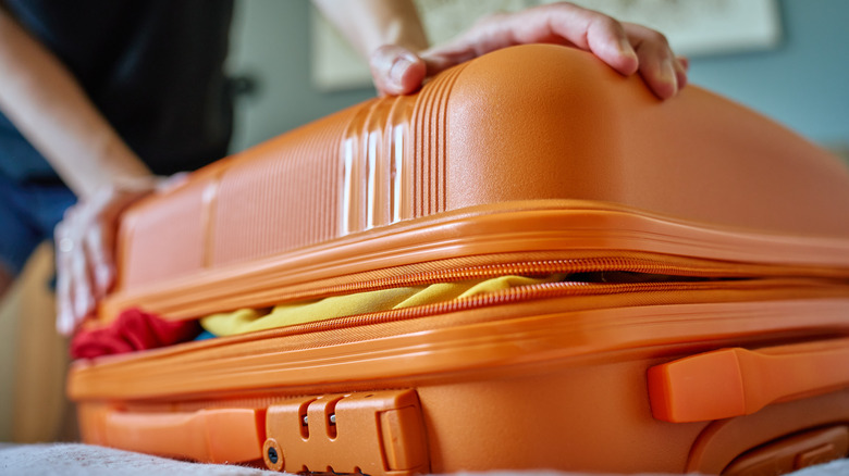 Person trying to close a stuffed, full suitcase