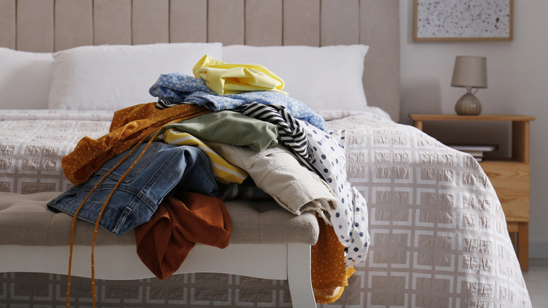 Messy pile of laundry sitting at the end of a bed