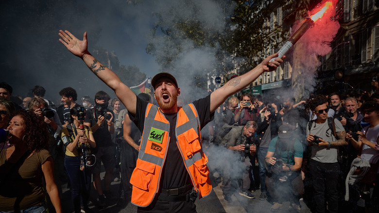 A member of the SUD Railway Union holds a flare aloft and chants as thousands of protesters march through central Paris