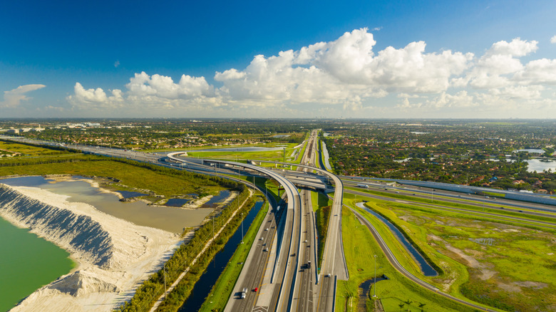 A mess of highway along I-75 viewed aerially with verdant grass with a bright blue sky full of cumulus clouds in Florida