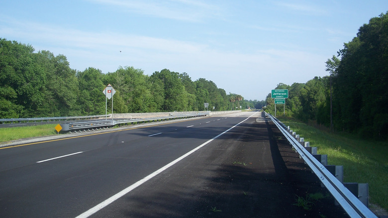 A big black stretch of highway with trees lining it and a big blue sky filled with faint cirrus clouds on U.S. 19 in Florida