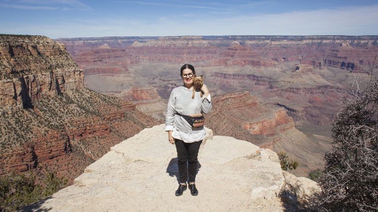 A woman stands with her small dog at the Grand Canyon