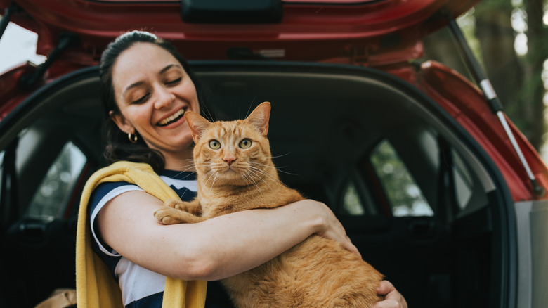 Woman holding orange cat seated at the back of a car