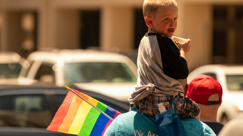 A young boy sitting on a man's shoulders holding a rainbow flag