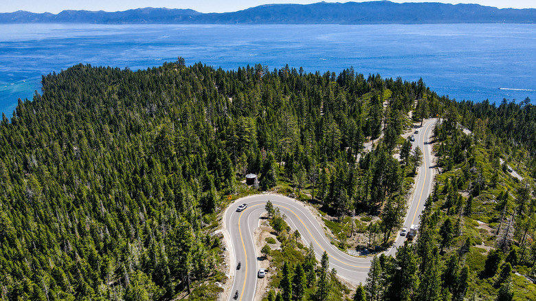 A windy road in a forest with a lake and mountains in the background