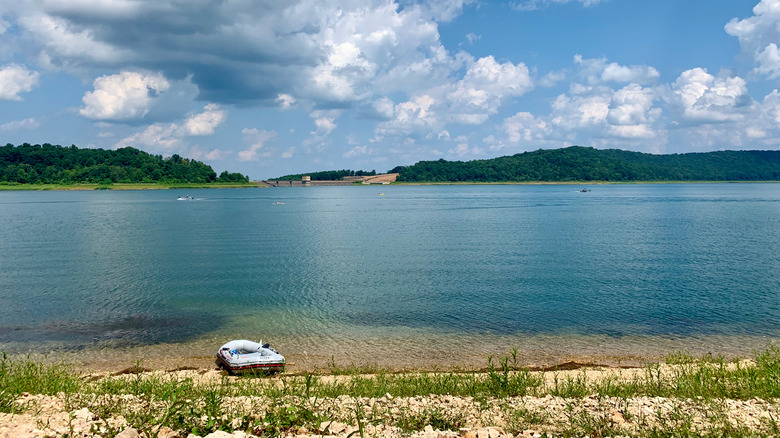 A raft on the sandy shores of a reservoir with green hills in the distance