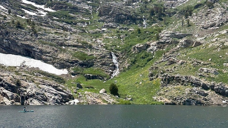A person paddles on a SUP board toward a waterfall at the edge of Angel Lake, Nevada