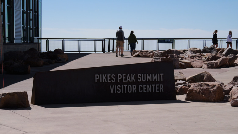 Visitors at the railing near a sign that reads "Pikes Peak Summit Visitor Center"