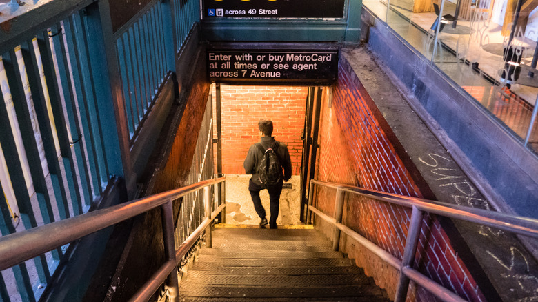 View down into lighted subway station in Manhattan at night with man on stairs