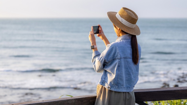 A woman taking a photo of the ocean
