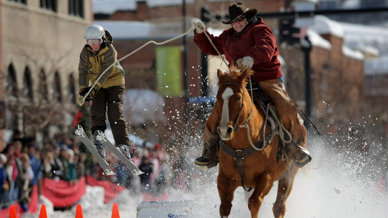 man on horse with rope pulling a skier who is jumping through the air