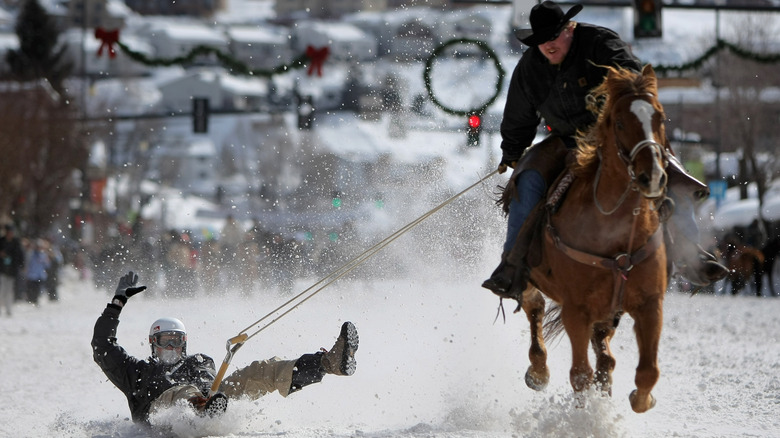 man on horse pulling a man riding a shovel through the snow