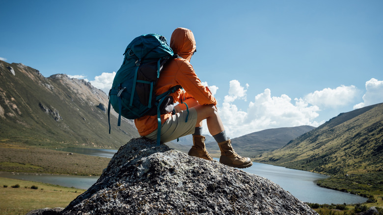 A hiker in an orange hiking jacket sits on a mountain