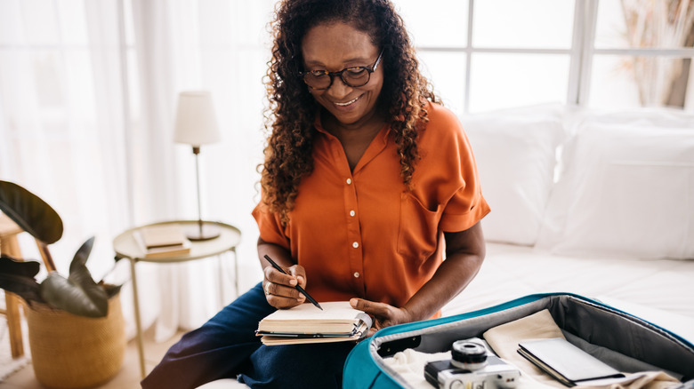 A smiling woman checks off her vacation packing list.