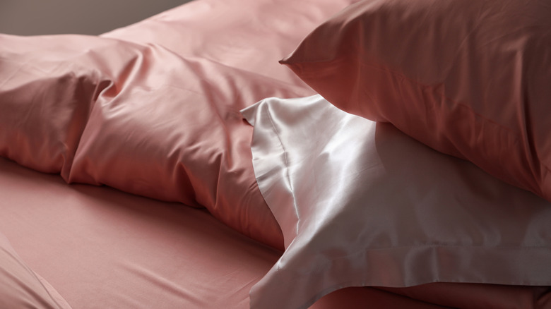 A bed with pink silk linens, including light pink pillowcases.