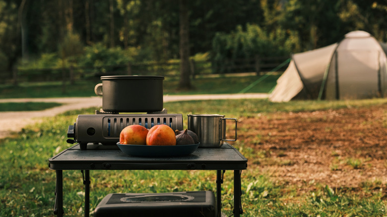 A single-burner camping stove set up outdoor with a large, black pot.