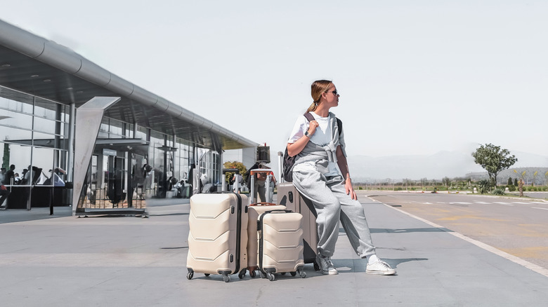 A woman sits alone with her luggage outside an airport
