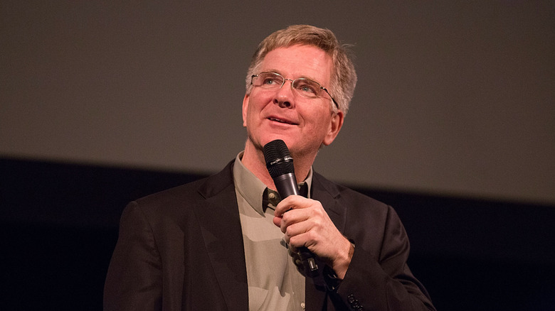 Rick Steves on stage while holding a microphone during a talk