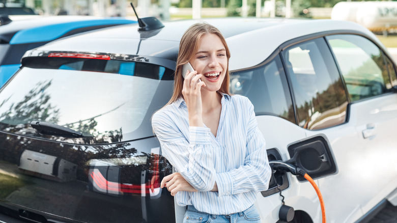 A young woman talking on the phone while charging her electric vehicle