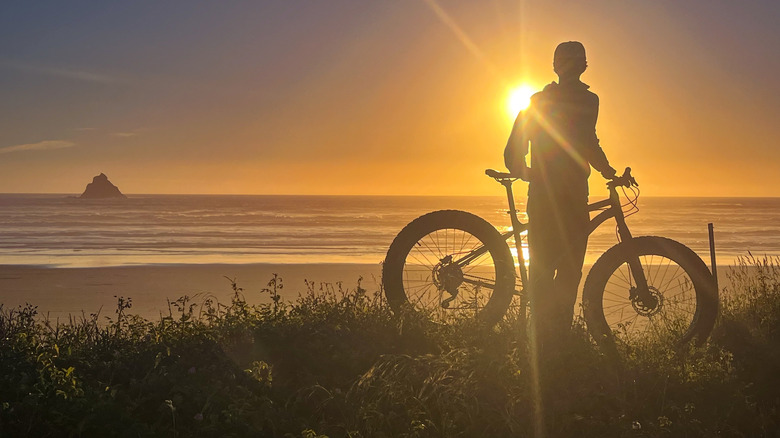 a silhouette of a man with a fat bike watching the sun set over the Oregon Coast