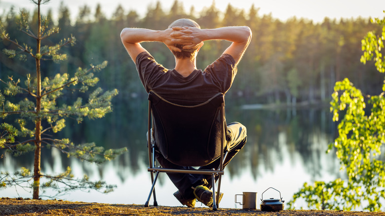 Man relaxes in camp chair by forested lake in Sweden