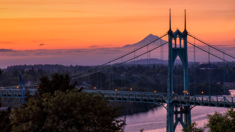 Sun sets behind Gothic arches of St. Johns Bridge in Portland with mountain on hhorizon