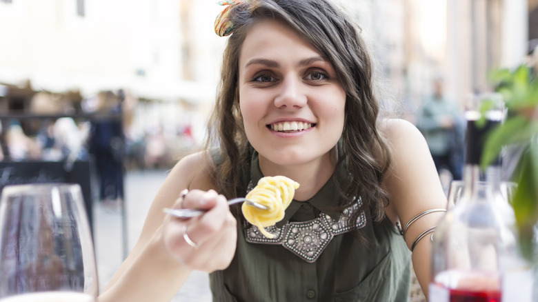 Smiling woman eating pasta in a blurry outdoor setting