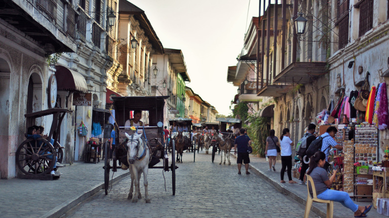 Street view of Vigan City with horse drawn carriages and people on both sides of the street.