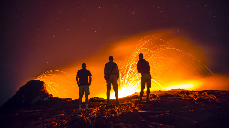 Three people standing at the edge of a volcano at night