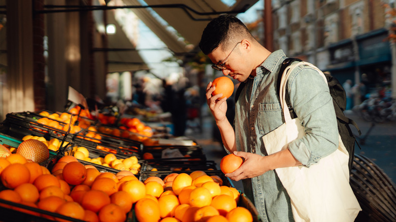 A man stops to smell oranges at a sidewalk stand