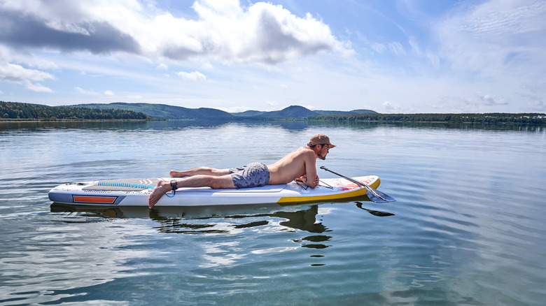 Young man relaxes on a paddleboard on a lake with mountains in the background.
