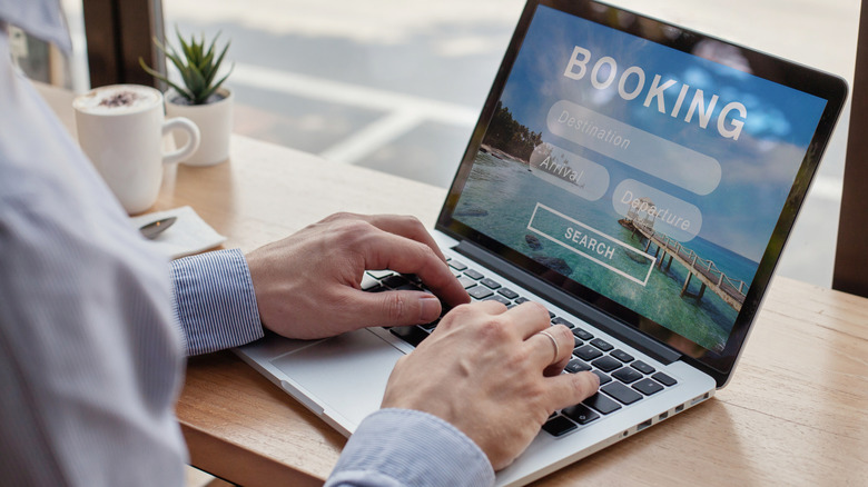 A man's hands on a laptop as he makes an online hotel booking.