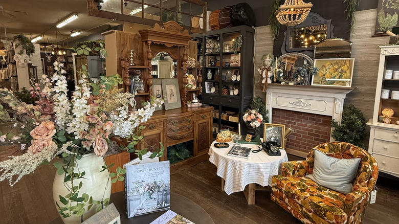 the interior of sparrow and nightingale vintage shop; a corner with a faux fireplace, a low table, an orange patterned fall leaf upholstered armchair, and a large chestnut colored credenza with various antique knick knacks about
