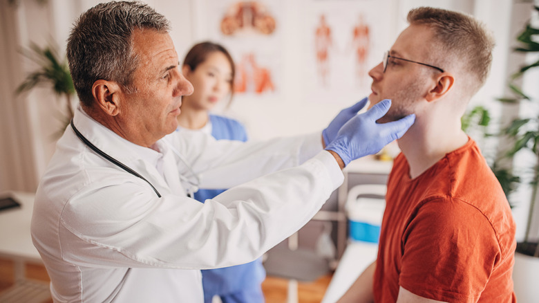 A man in an orange shirt being examined by a doctor with nurse in the background
