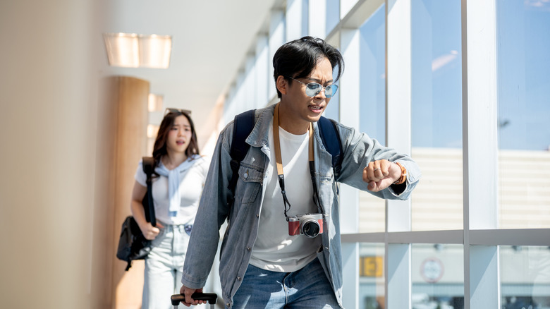 two people running through airport while checking their watches to make flight