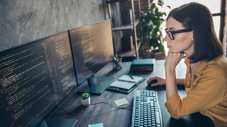 Woman with chin on hand looking at two monitors in office