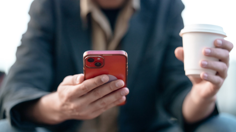 Closeup of man holding red phone in right hand and white coffee cup in left